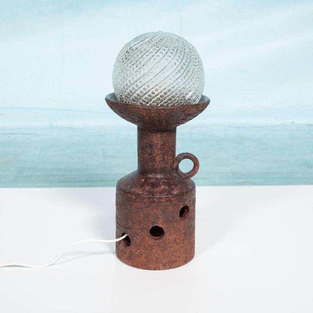 Subtly designed table lamp from the sixties made of ceramic and a semi-transparent glass ball with relief. The natural-...