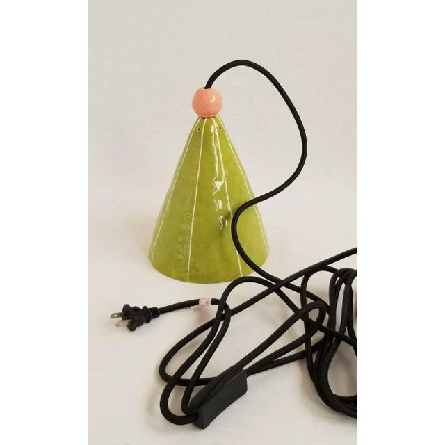 Simple cone shaped pendant light glazed in moss green is handmade. Detailed with a peach-pink accent bead and thin, raised...