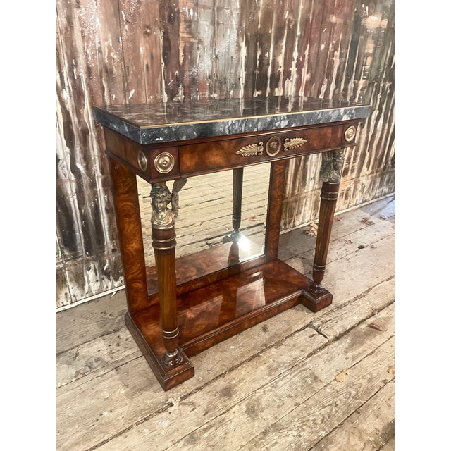 A beautiful Neo-Classic-style console table in figured walnut with a brass bordered mottled stone top and a mirrored back....
