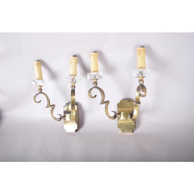 Matched pair of 1950s brass wall sconces attributed to Jules Leleu. Each has two scrolled brass arms extending from a...