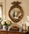 A Federal-style giltwood convex mirror crowned with a carved eagle, its wings outstretched above a laurel motif—an...