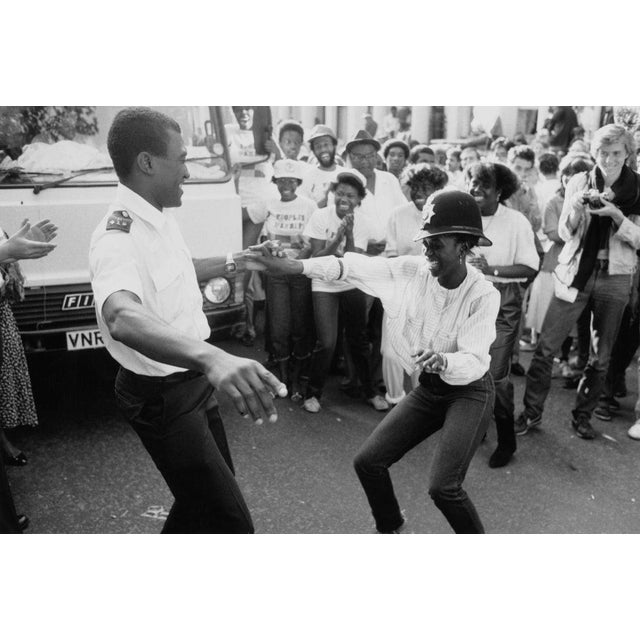 Notting Hill Carnival A policeman dancing with a reveller, who is wearing his hat, surrounded by the crowd at the Notting...