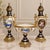 Elegant three-piece French-style porcelain garniture set featuring two matching covered vases and a coordinating central...