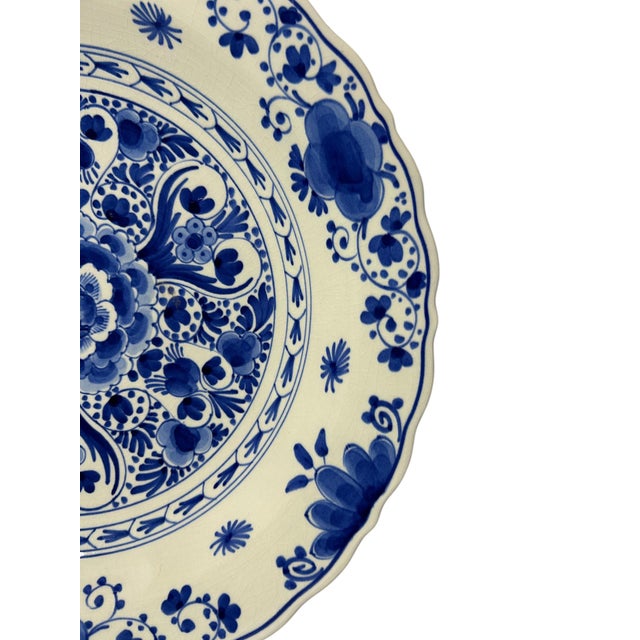 A vintage royal delft wall plate, hand-painted in delft blue with a dense floral centre, a scalloped rim and a decorative...