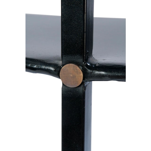 A graduated etagiere with four half round shelves. Glossy black painted finish metal with natural brass details. Top shelf...