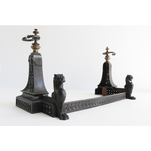 An elegant 19th century French fireplace set consisting of two finely cast chenets, joined by a decorative fender bar....