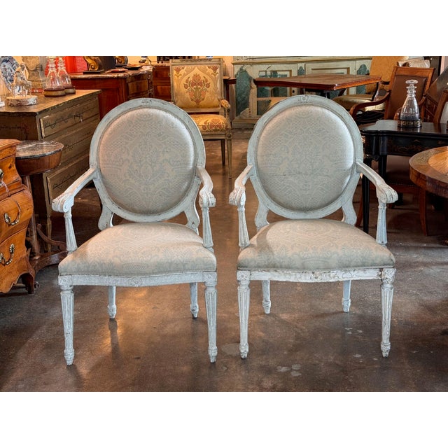 A pair of 19th century Louis XVI style armchairs in a soft dove-blue painted finish, each with an oval medallion back...
