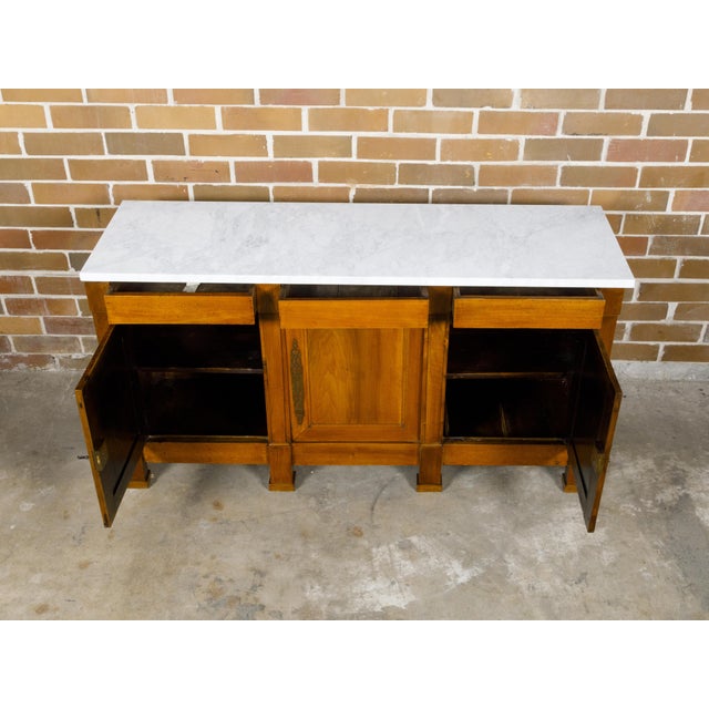 A French walnut enfilade from the 19th century with white marble top, three drawers over three doors and Doric pilasters....