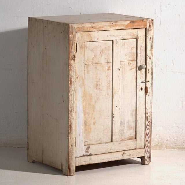 This antique cupboard in pine wood is a Central European rustic cabinet with a single door, a porcelain knob and worn...