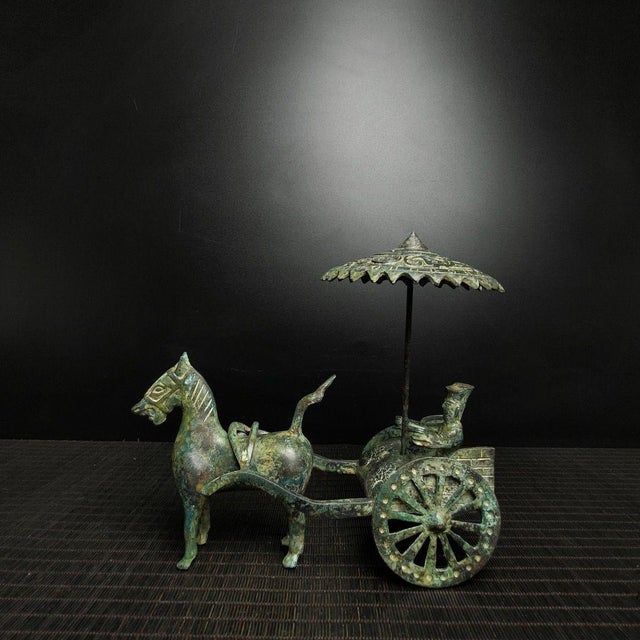 A striking Chinese bronze sculpture of a horse-drawn chariot. The piece features a stylized horse with a raised tail...
