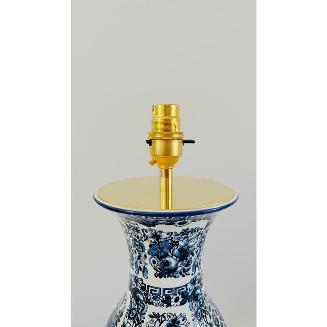 A 20th century table lamp made from a baluster shaped delfia vase. The white lamp is decorated with lush flowers, leaves...