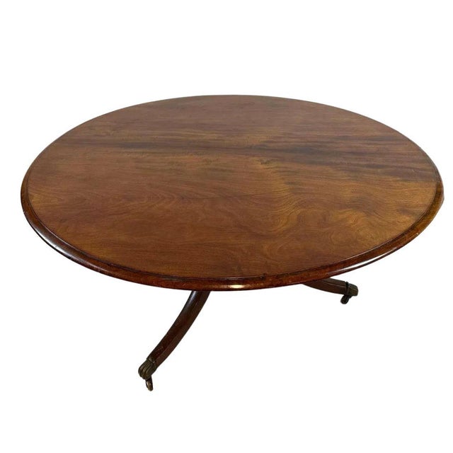 A vintage Regency style mahogany round dining table with a tripod pedestal base, ending on casters.