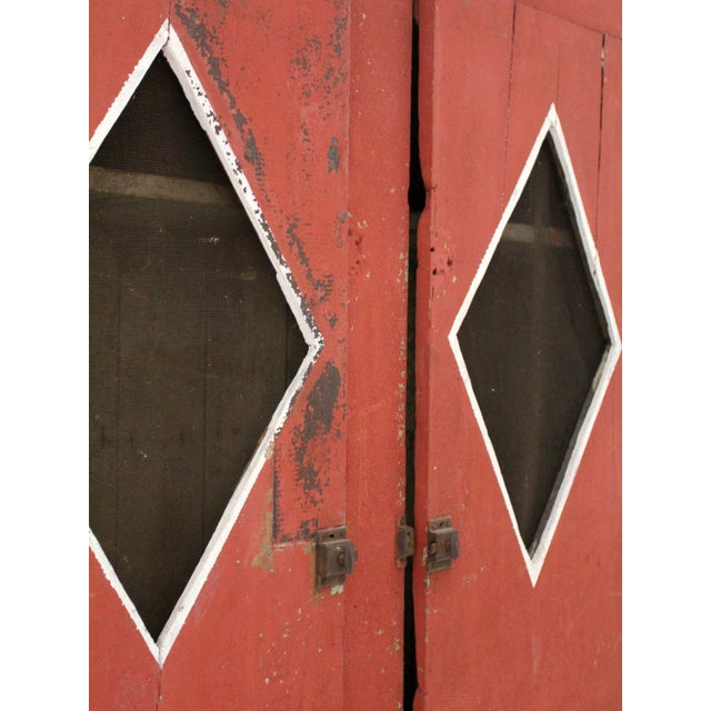 This antique primitive cabinet has original red paint and diamond-pattern screen windows on the doors. Likely a pie safe...