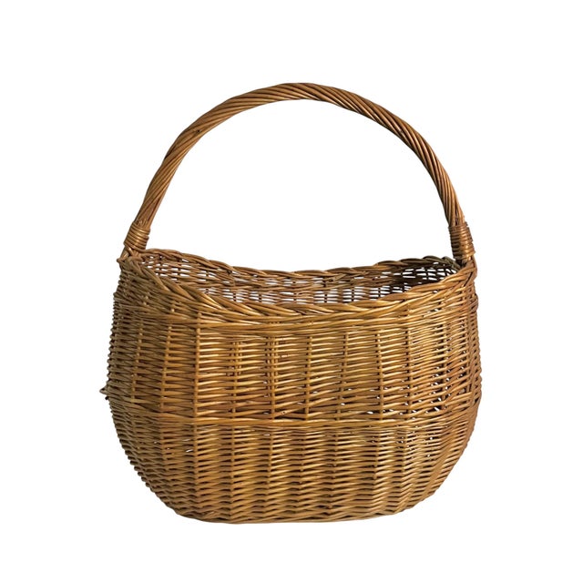 A beautiful early 20th-century French wicker gathering basket featuring a gracefully arched handle and rich honey-colored...