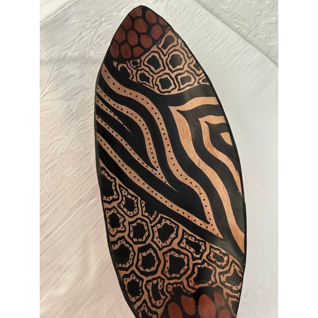 Vintage artisanal African carved wood canoe shaped shallow bowl in earth-tone shades featuring a hand-painted decorative...