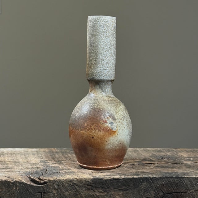 A vintage Modernist wood fired stoneware vase with a tall cylindrical neck and rounded base. The surface has sections of...
