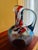 This sculptural hand-blown glass pitcher features a striking abstract composition of blue, amber, red, and cobalt...
