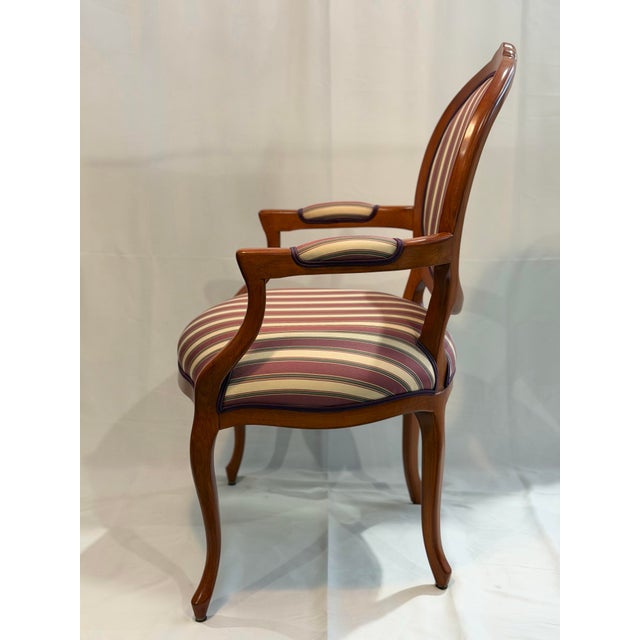 A refined Louis XVI style armchair featuring the classic oval back silhouette and gracefully curved arms. The warm...