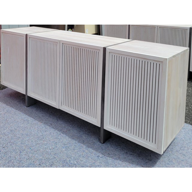 Cast aluminum legs/dividers and narrow slatted doors define this four-door white-washed solid acacia credenza from...
