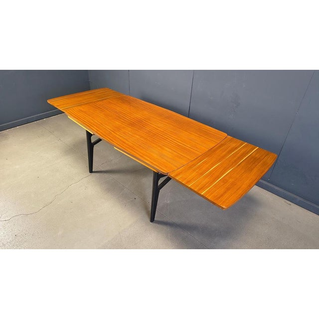 Elegant italian mid century dining table. The dining table has two extractable table tops and a black ebonized wooden base...