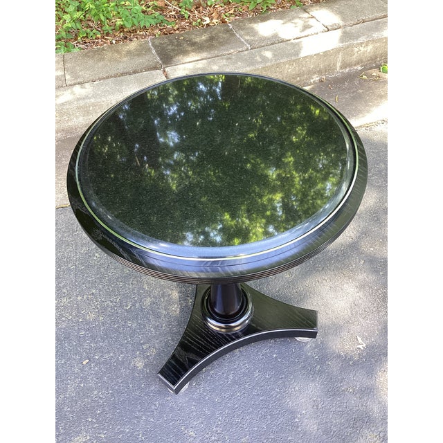 A refined neoclassical-style guéridon side table featuring a polished black marble top set within a sleek ebonized wood...