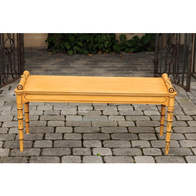 An English vintage painted wooden bench from the mid-20th century, with cylindrical armrests and faux bamboo legs. Born in...