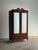 Antique mahogany wardrobe cabinet with mirrored doors and a shaped scroll crest, the surface showing warm red-brown tones...
