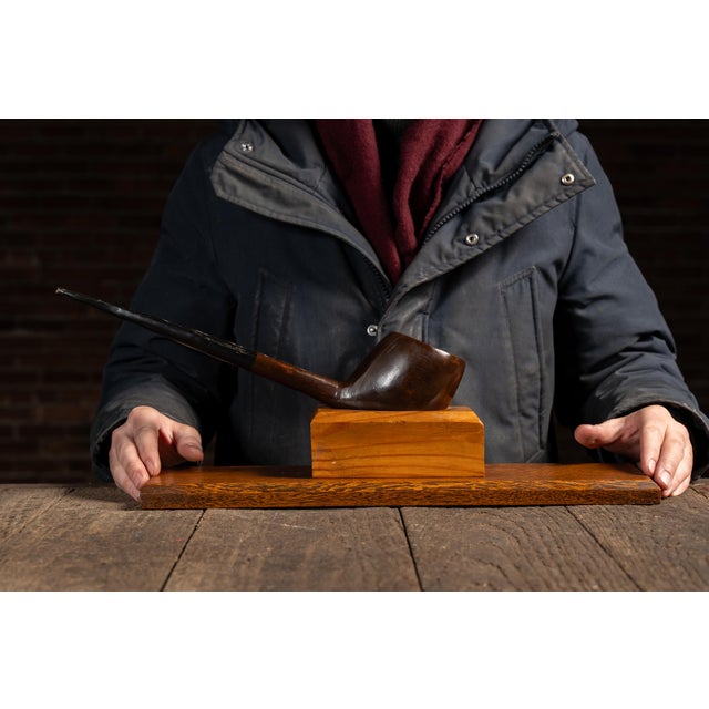 Figural wooden pipe rack designed in the form of an oversized long-stemmed tobacco pipe, with the stem drilled to accept...