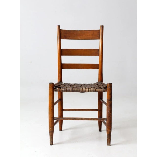 This antique American splint weave chair boasts a classic rustic design. The warm russet brown ladder back frame with...