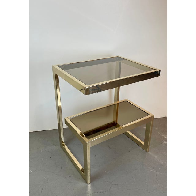 Elegant hollywood regency side table crafted in gold-plated metal, featuring a distinctive g-shaped structure that gives...