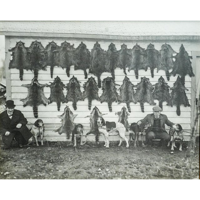 This evocative black-and-white photograph captures a moment from a bygone era, showcasing two men and their hunting dogs...