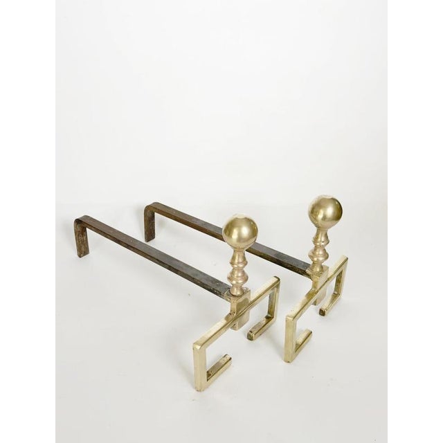 Elegant pair of French andirons featuring polished brass fronts with spherical finials and sturdy cast iron log supports....
