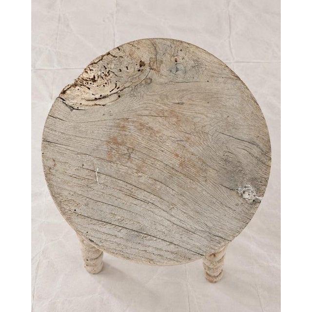 A rustic tripod stool with a thick solid wood circular seat set over three splayed, bobbin-turned spindle legs. The...