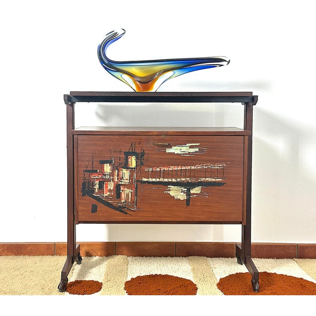 A mobile bar on wheels, an icon of mid-century Italian lifestyle. The piece features a warm-toned wooden structure,...