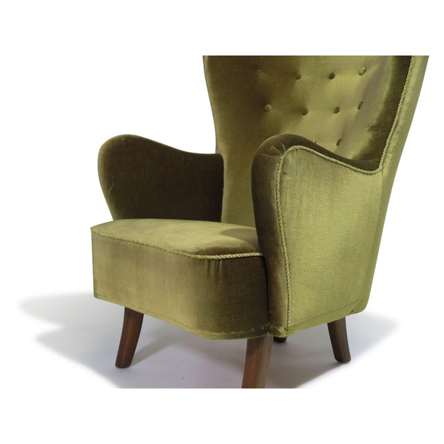 1950s Danish high-back lounge chair constructed with a solid wood frame in a curved form, featuring hand-tied springs and...