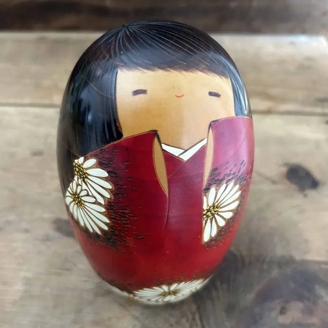 Beautifully stylized kokeshi crafted by the renowned Usaburo. The kokeshi wears a red kimono adorned with a daisy motif...
