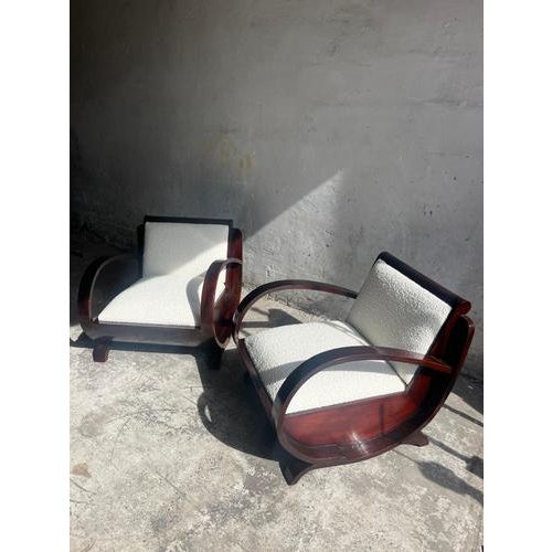 This elegant pair of Art Deco club chairs showcases a sculptural design with beautifully curved wooden armrests and a...