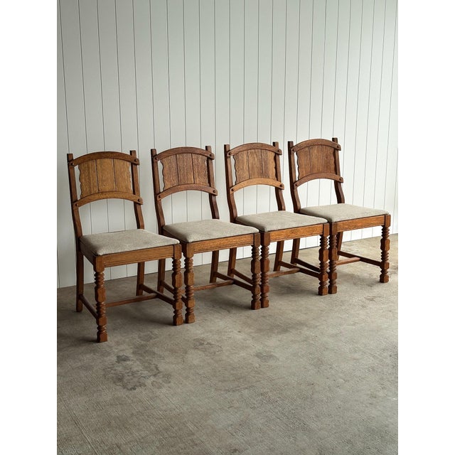 Antique English dining chairs crafted in solid oak with arched pegged backs, carved splats, and turned legs. Warm, time-...