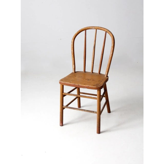 An antique farmhouse Windsor dining chair dating to the late 19th century. The painted wood chair features a gracefully...