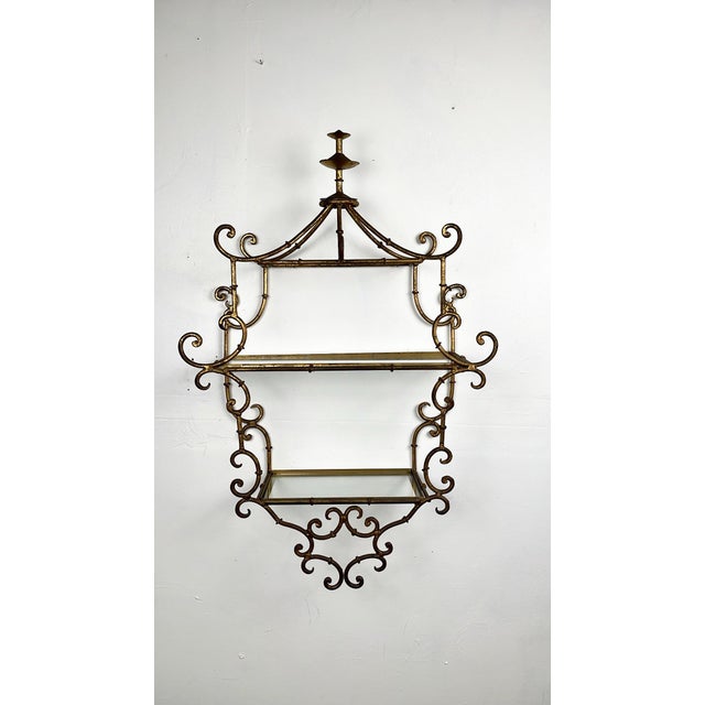Vintage chinoiserie gilt metal wall shelf. Wonderful gold ornate scrollwork frame with stylized pagoda top. Two glass...