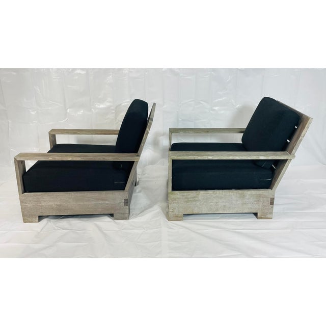 A pair of solid teak patio armchairs by Restoration Hardware, designed with bold architectural lines and generous...