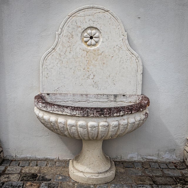 Wall fountain made of light Giallo d’Istria limestone with a brown-patinated basin rim. The back panel features a simple...