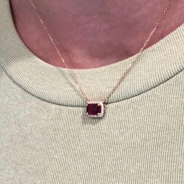This beautiful pendant necklace features a 1.6 carat emerald cut ruby gemstone with a halo of natural earth mined...