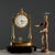 Neoclassical-style table clock in gilded and chiseled bronze. A pair of turned columns support the enameled metal dial...