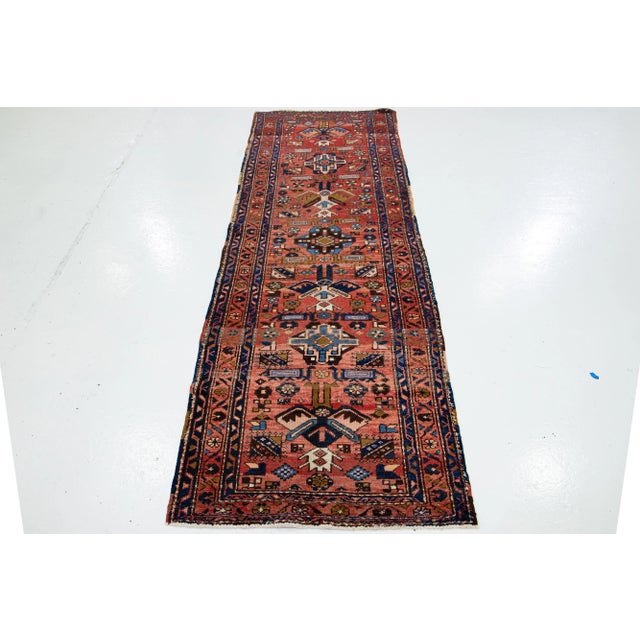 This vintage Persian Hand-knotted Heriz Runner has a red field with multicolor accents all over the tribal motif. This rug...