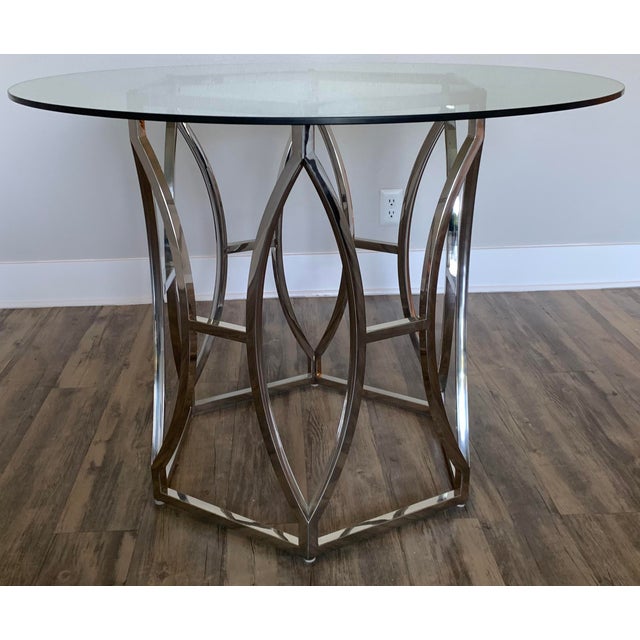 Couture Glass Top Round Dining Table featuring an intricate geometric stainless steel base and a clear floating glass top