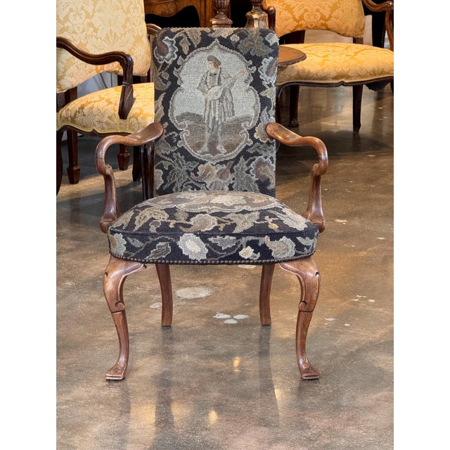 A walnut armchair on cabriole legs with pad feet and scrolled arms. The needlepoint upholstery features a floral ground...