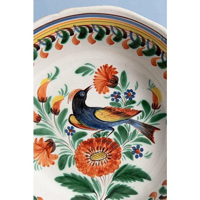 An early 19th-century French faience serving bowl from Quimper, decorated with a colourful bird perched on sprays of...