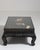 A decorative coffee table inspired by Chinoiserie motifs, featuring a glass top that highlights the detailed base. The...