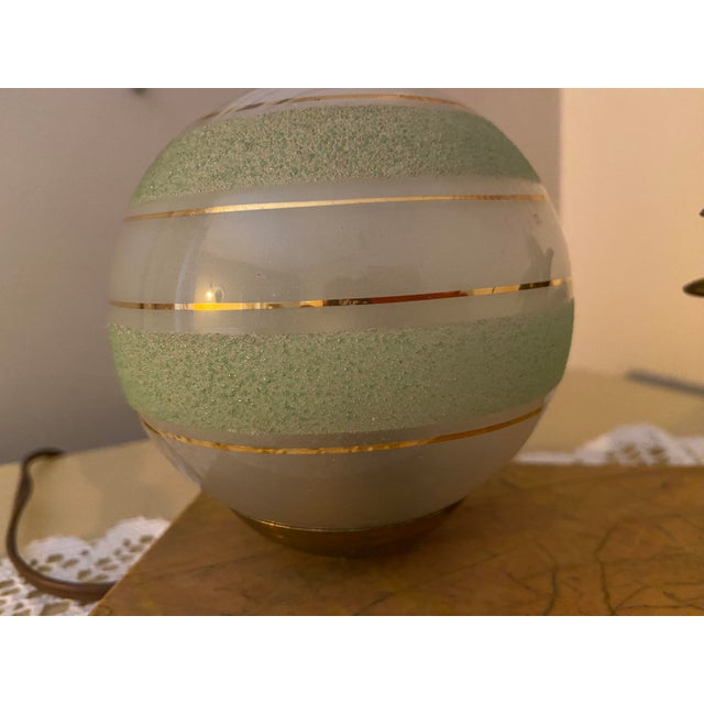 An elegant vintage decorative table lamp featuring a beautifully sculpted bird in flight, an illuminated spherical glass...